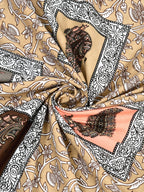 Swirled fabric close-up of a peach peacock patch on a sand-beige floral vine print