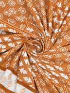 Swirled fabric close-up of white leaf and flower butas on a rust orange striped background