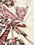 Swirled fabric close-up of maroon, rust, pink and brown leaf motifs on a cream lattice-textured base