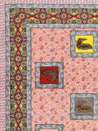 Close-up of yellow, red and grey peacock patches on a peach floral vine background with maroon border