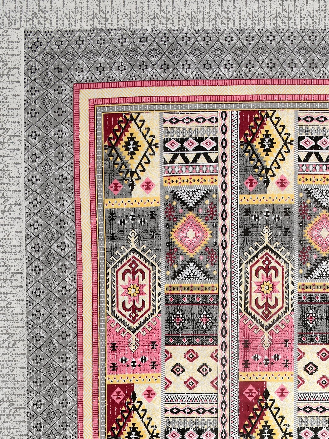 Corner close-up of rose pink, maroon, butter yellow and black kilim-style panels and the grey geometric border