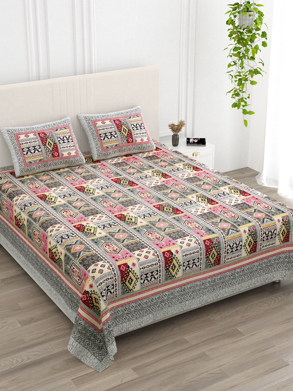 Angled view of the pink & grey Aztec patchwork bedsheet on a bed with 2 pillow covers