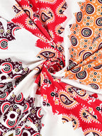 Swirled fabric close-up of red, peach and wine paisley print on white
