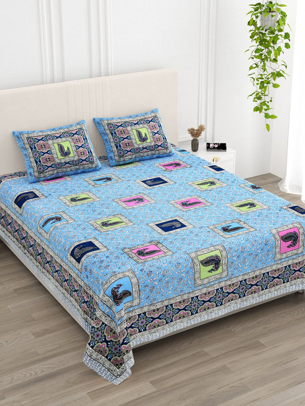 Angled view of the sky blue peacock print bedsheet in a bright bedroom with an indoor plant