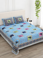 Angled view of the sky blue peacock print bedsheet in a bright bedroom with an indoor plant